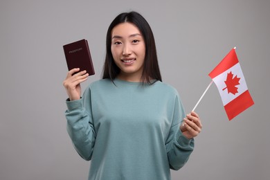 Immigration to Canada. Happy woman with passport and flag on grey background