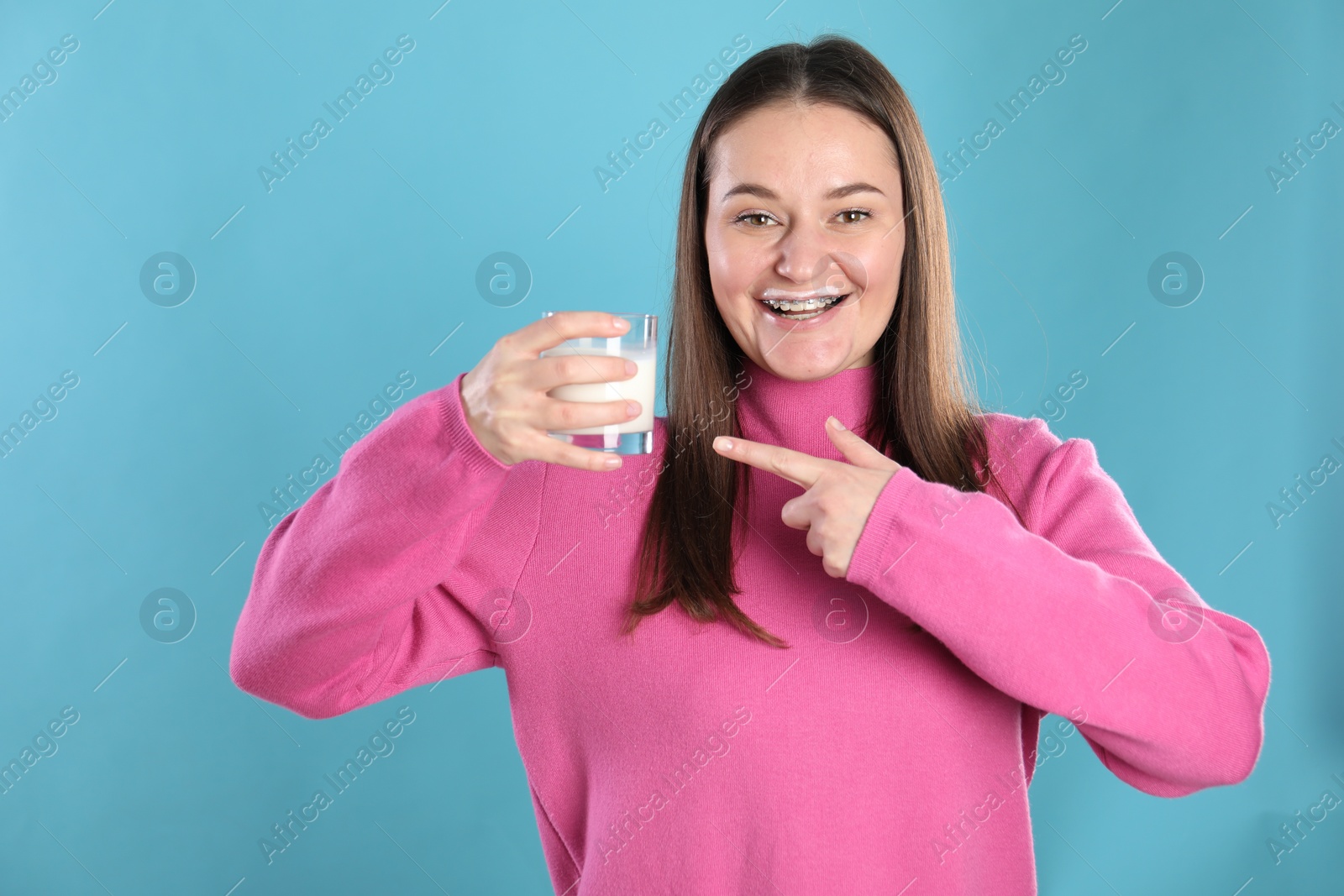 Photo of Happy woman with milk mustache pointing at glass of drink on light blue background