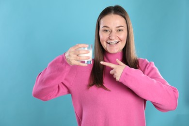 Happy woman with milk mustache pointing at glass of drink on light blue background