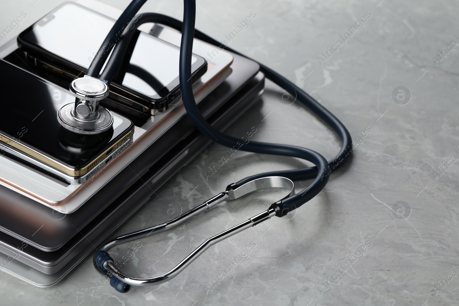 Photo of Stack of electronic devices and stethoscope on grey table, closeup