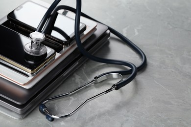 Photo of Stack of electronic devices and stethoscope on grey table, closeup