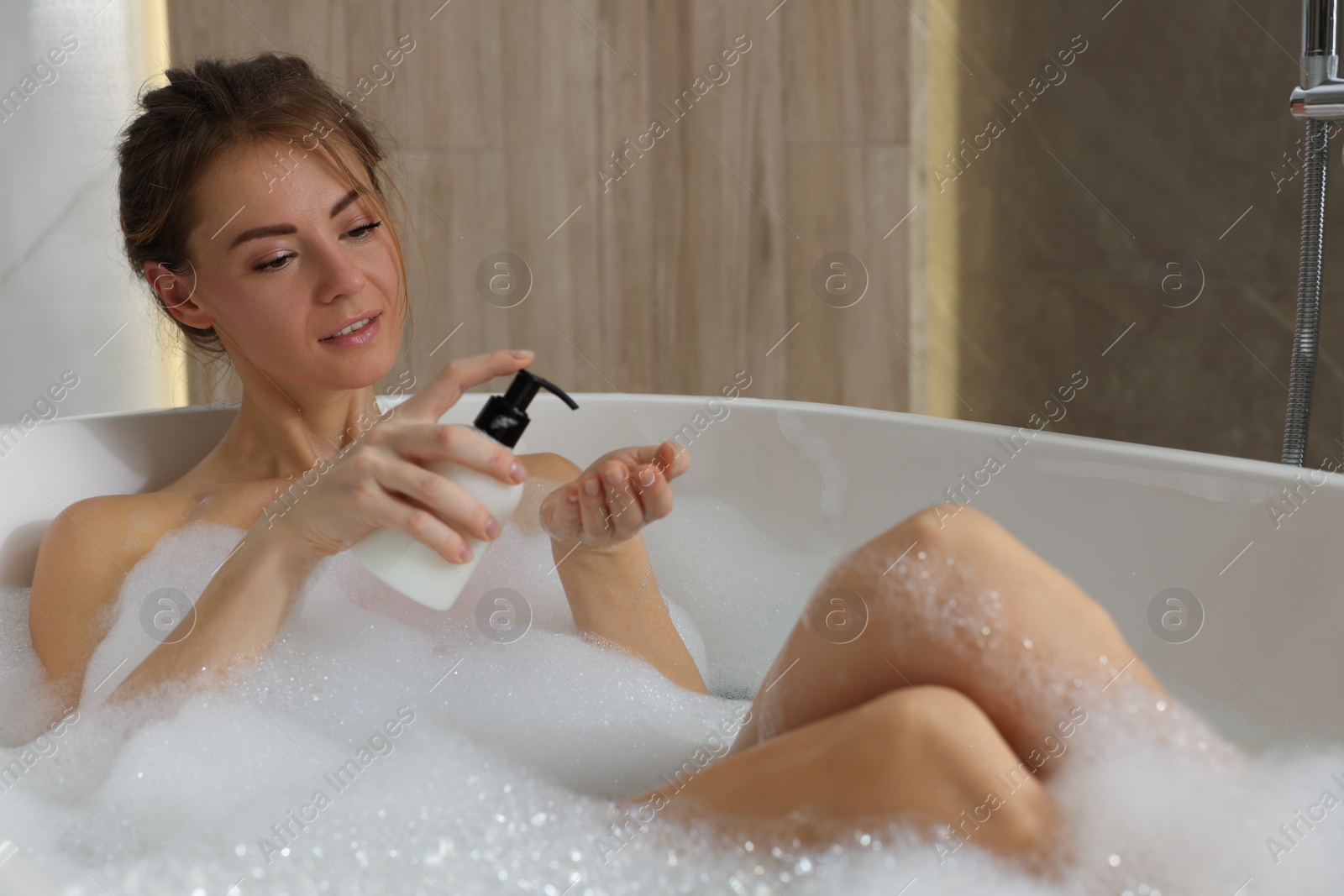 Photo of Beautiful woman pouring shower gel onto hand in bath indoors