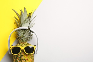 Funny pineapple with headphones and sunglasses on color background, top view. Space for text