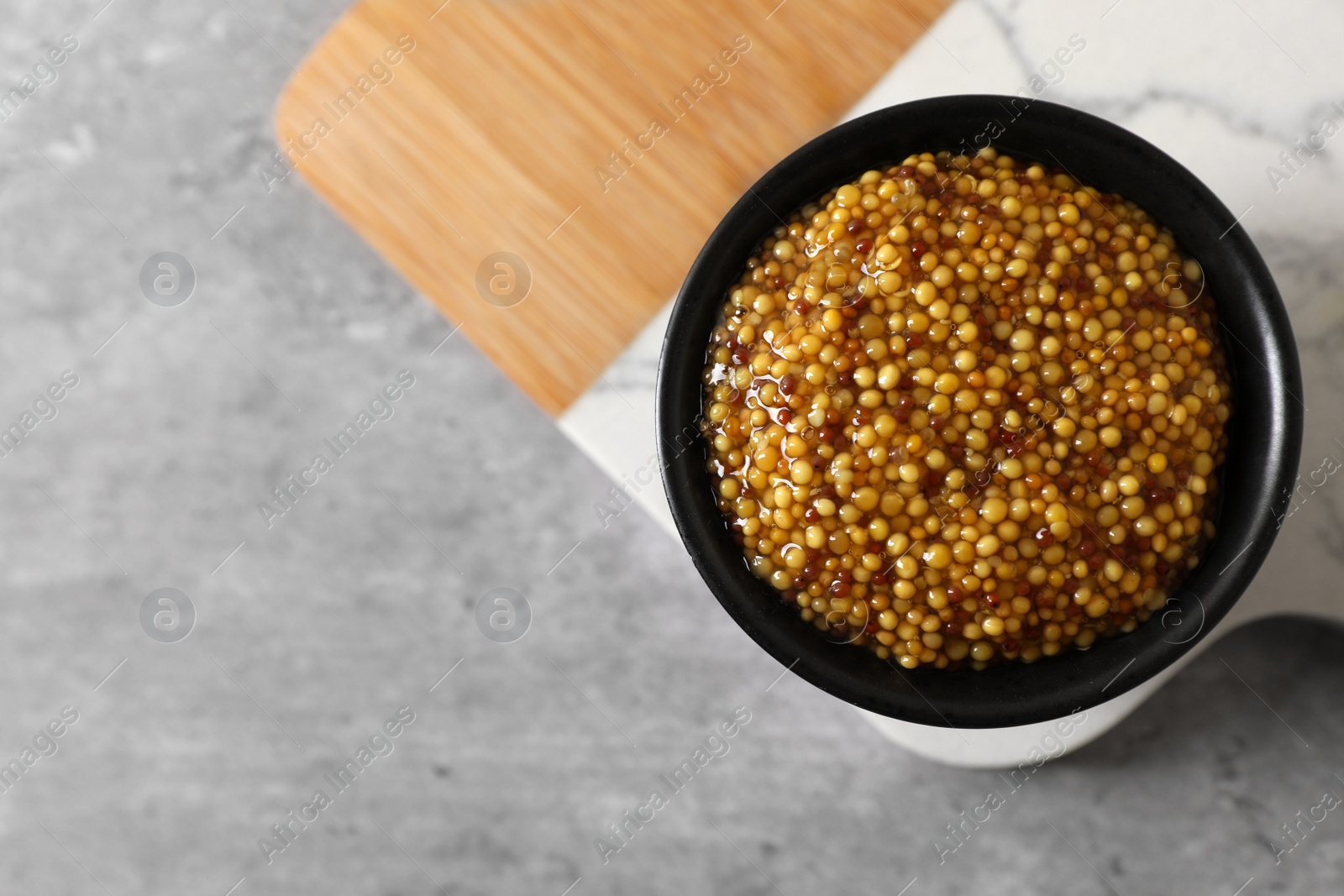 Photo of Wooden board with bowl of delicious whole grain mustard on grey table, top view. Space for text