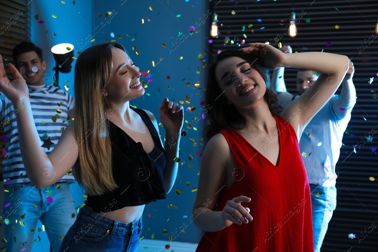 Photo of Happy friends and falling confetti in dark room