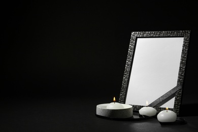 Photo of Funeral photo frame with ribbon and candles on black background. Space for design
