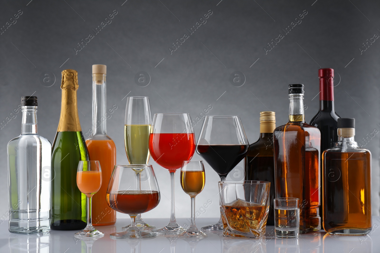 Photo of Bottles and glasses with different alcoholic drinks on table against gray background