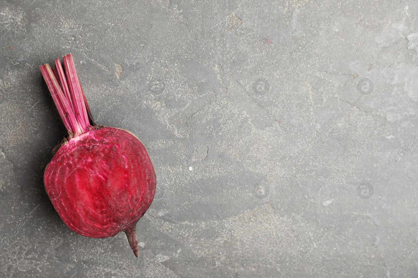 Photo of Half of raw beet on grey table, top view. Space for text