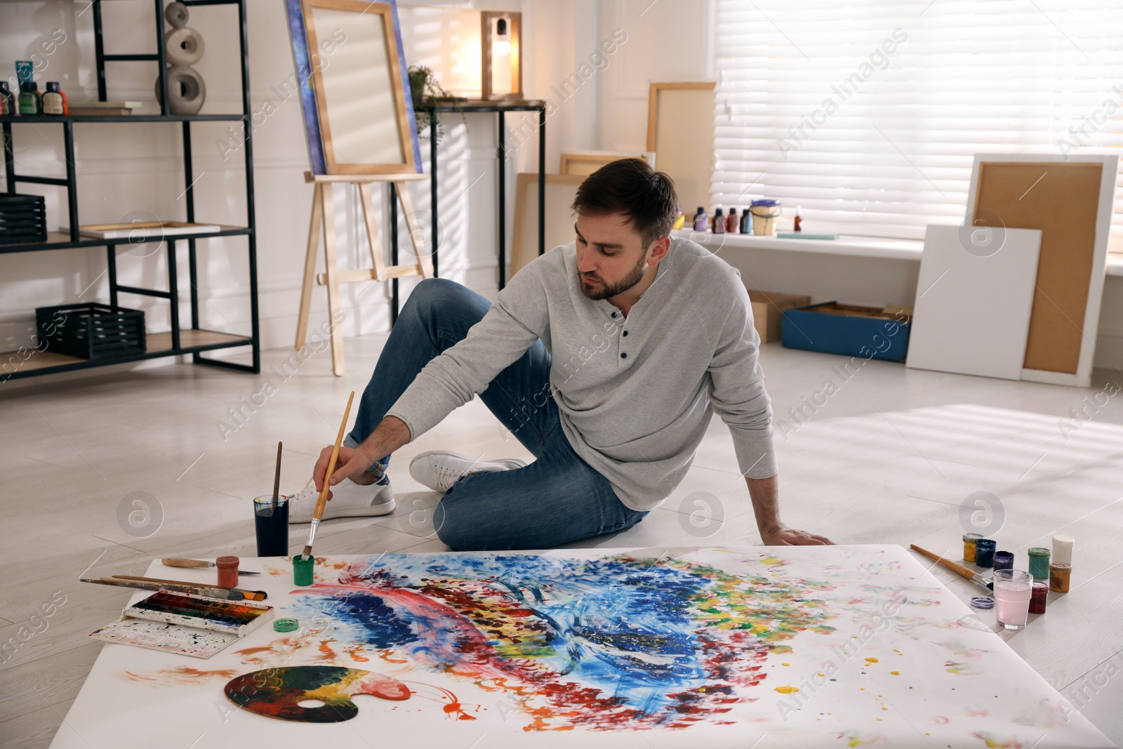 Photo of Young man painting on canvas with brush in artist studio