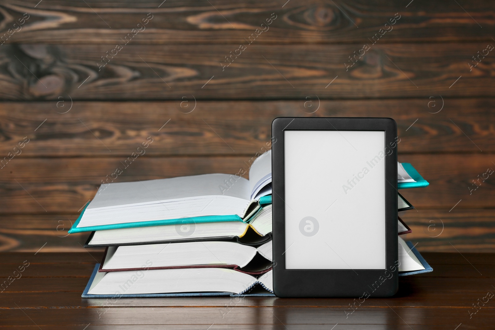 Photo of Portable e-book reader and many hardcover books on wooden table