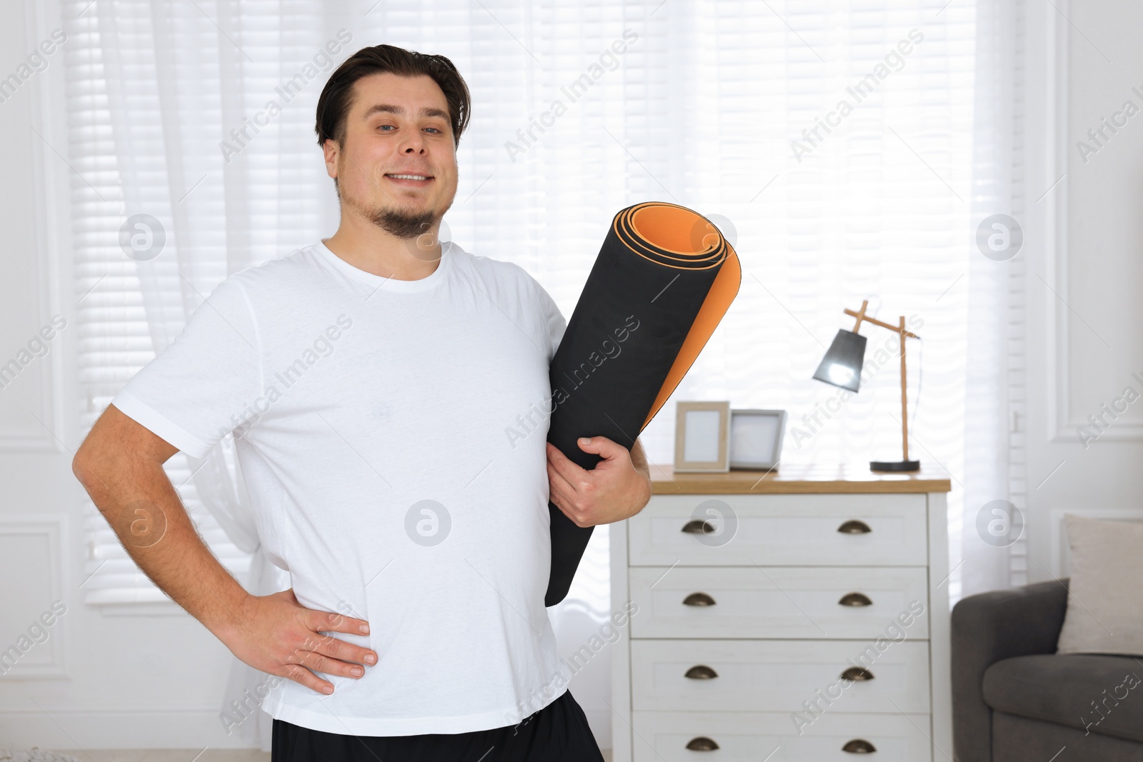 Photo of Overweight man with yoga mat at home, space for text