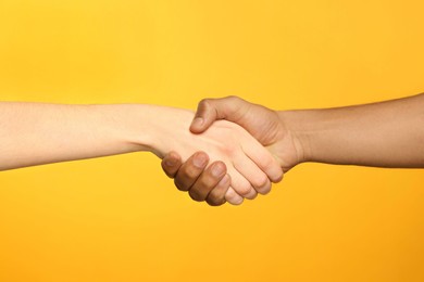 Photo of International relationships. People shaking hands on orange background, closeup