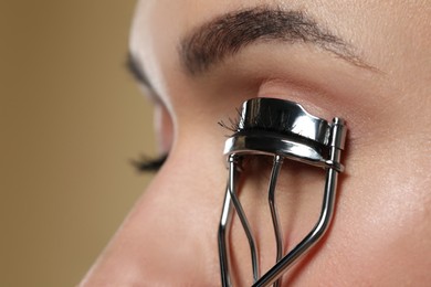 Photo of Woman using eyelash curler on beige background, closeup. Space for text