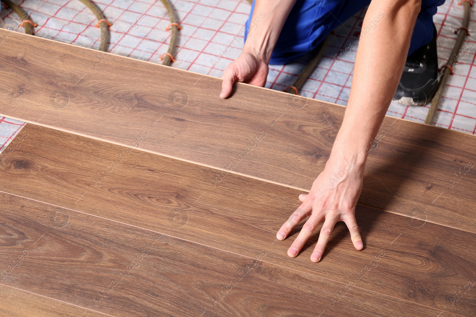 Photo of Worker installing new wooden laminate over underfloor heating system, closeup