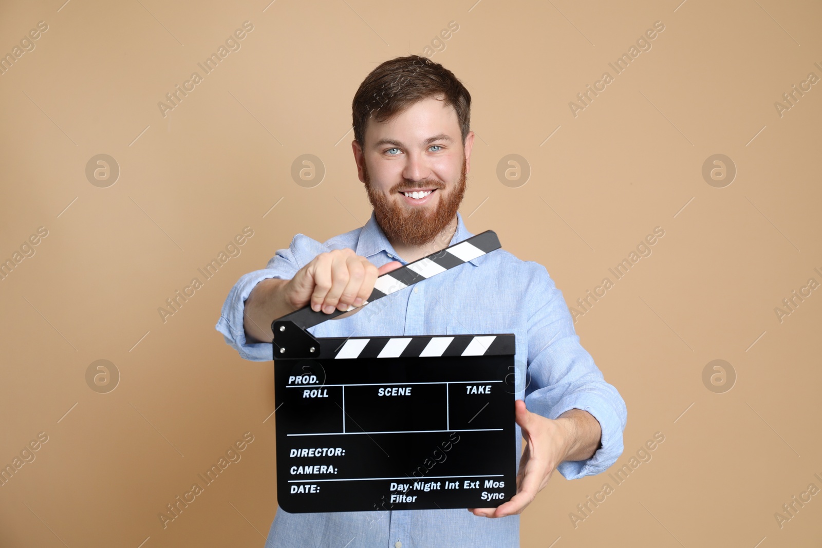 Photo of Making movie. Smiling man with clapperboard on beige background