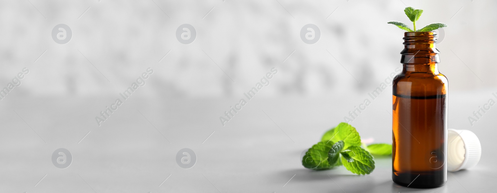 Image of Bottle with mint essential oil on table, space for text. Banner design