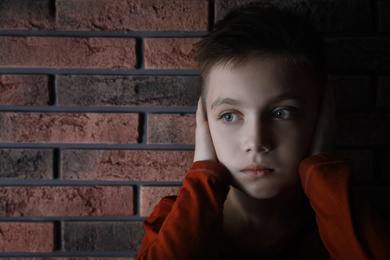 Photo of Sad little boy closing his ears near brick wall. Domestic violence concept