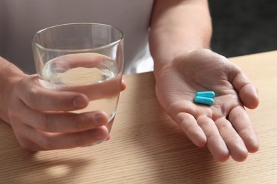 Photo of Man with glass of water and pills at wooden table, closeup