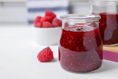 Photo of Delicious jam and fresh raspberries on white table, closeup. Space for text