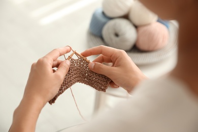 Photo of Young woman knitting with needles indoors, closeup. Engaging in hobby