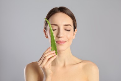 Photo of Young woman with aloe leaf on light grey background