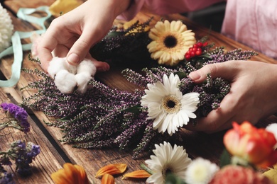 Photo of Florist making beautiful autumnal wreath with heather flowers at wooden table, closeup