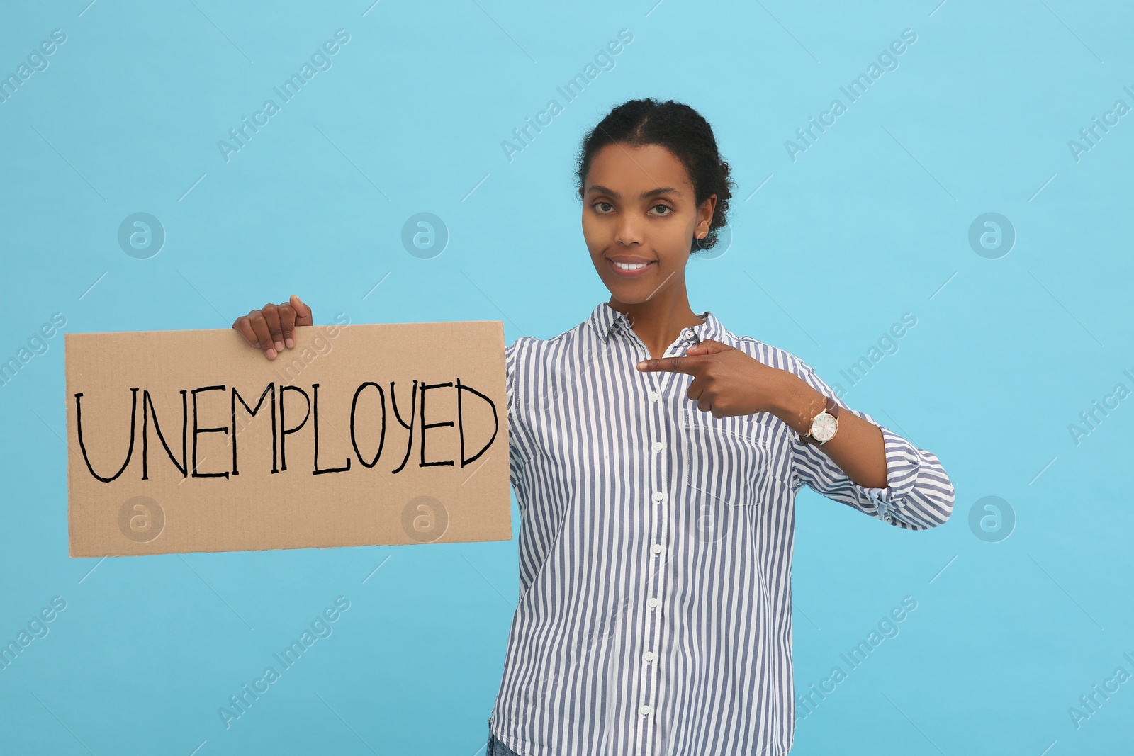 Photo of African American woman holding sign with word Unemployed on light blue background