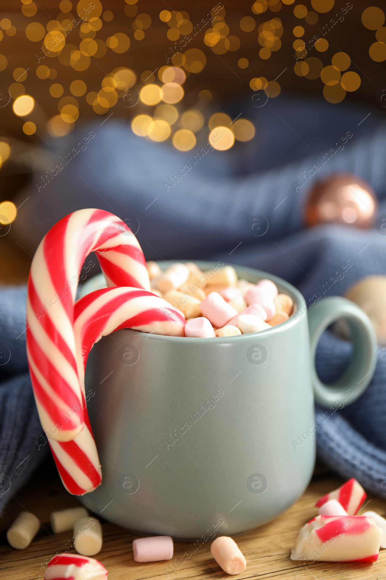 Photo of Cup of tasty cocoa with marshmallows and Christmas candy canes on wooden table against blurred festive lights