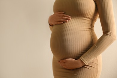 Photo of Pregnant woman touching her belly on beige background, closeup. Space for text