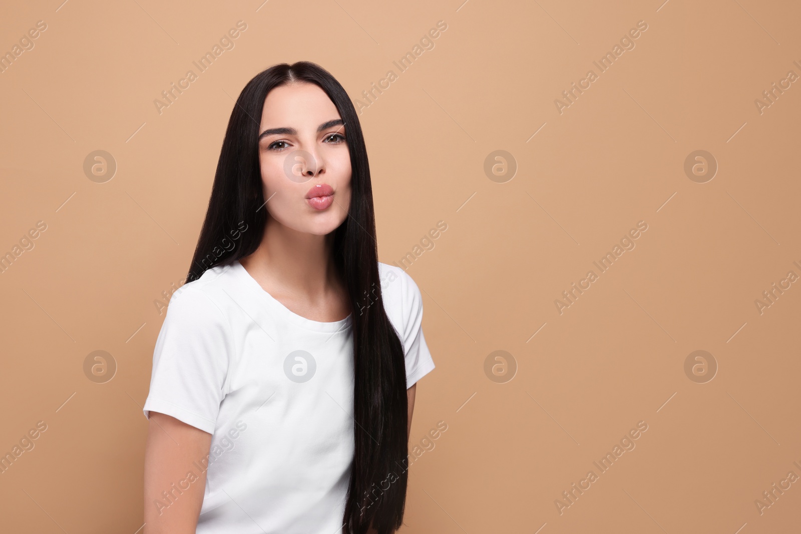 Photo of Beautiful young woman blowing kiss on beige background. Space for text