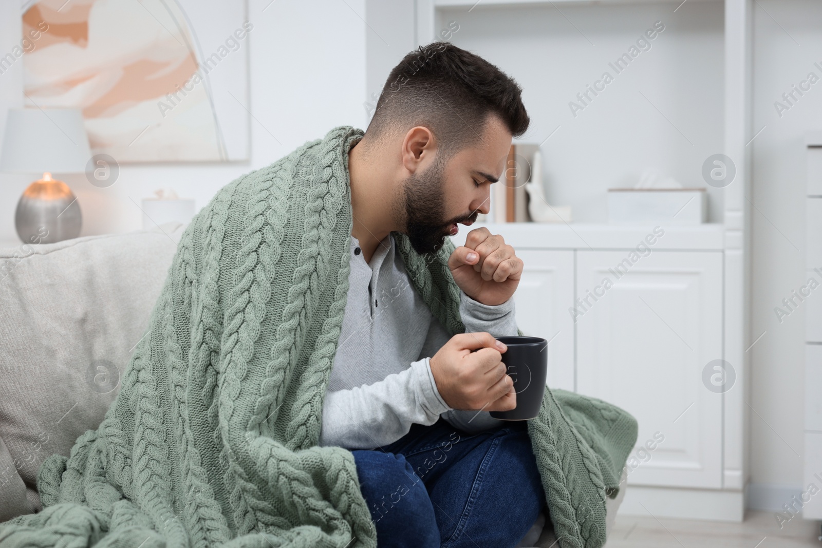 Photo of Sick man with cup coughing at home