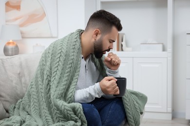 Sick man with cup coughing at home