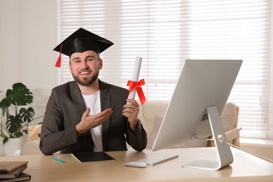 Photo of Happy student with graduation hat and diploma at workplace in office