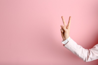 Young woman showing victory gesture on color background. Space for text