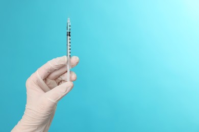 Doctor holding syringe on light blue background, closeup. Space for text