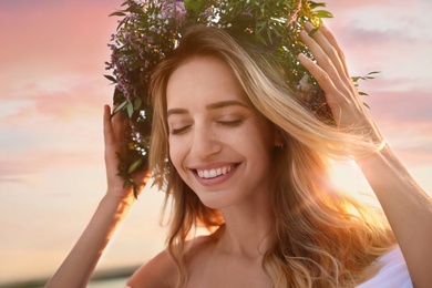 Photo of Young woman wearing wreath made of beautiful flowers outdoors