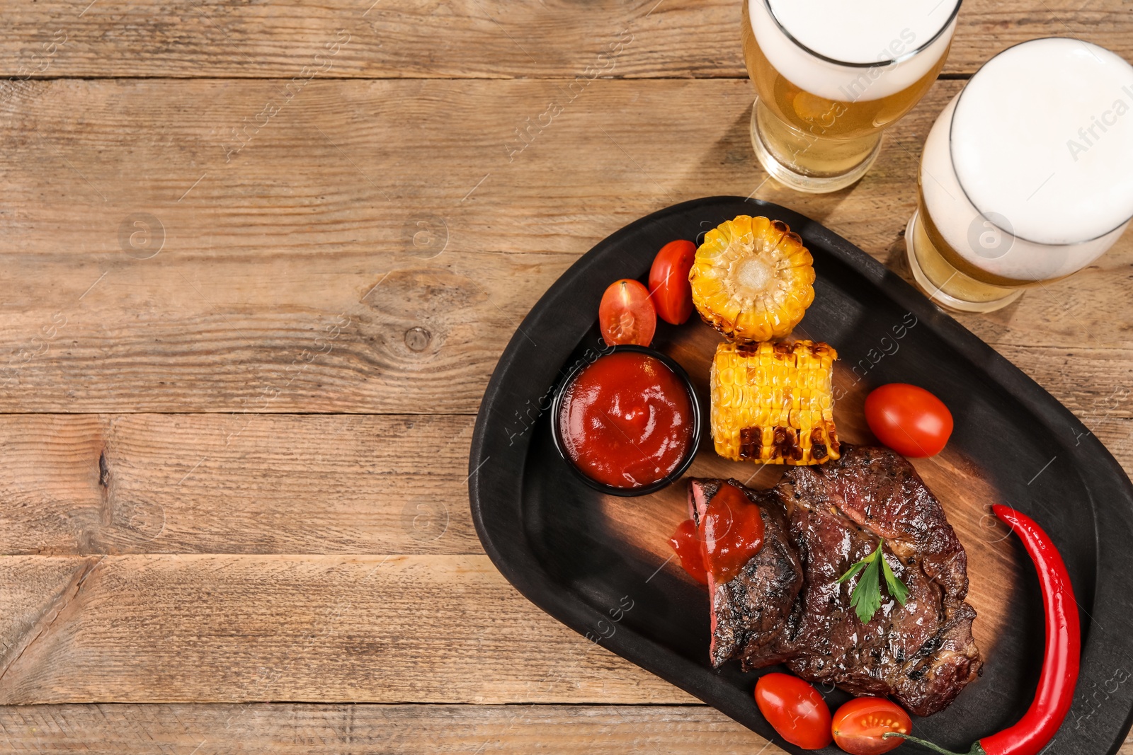 Photo of Glasses of beer, delicious fried steak and ingredients on wooden table, flat lay. Space for text