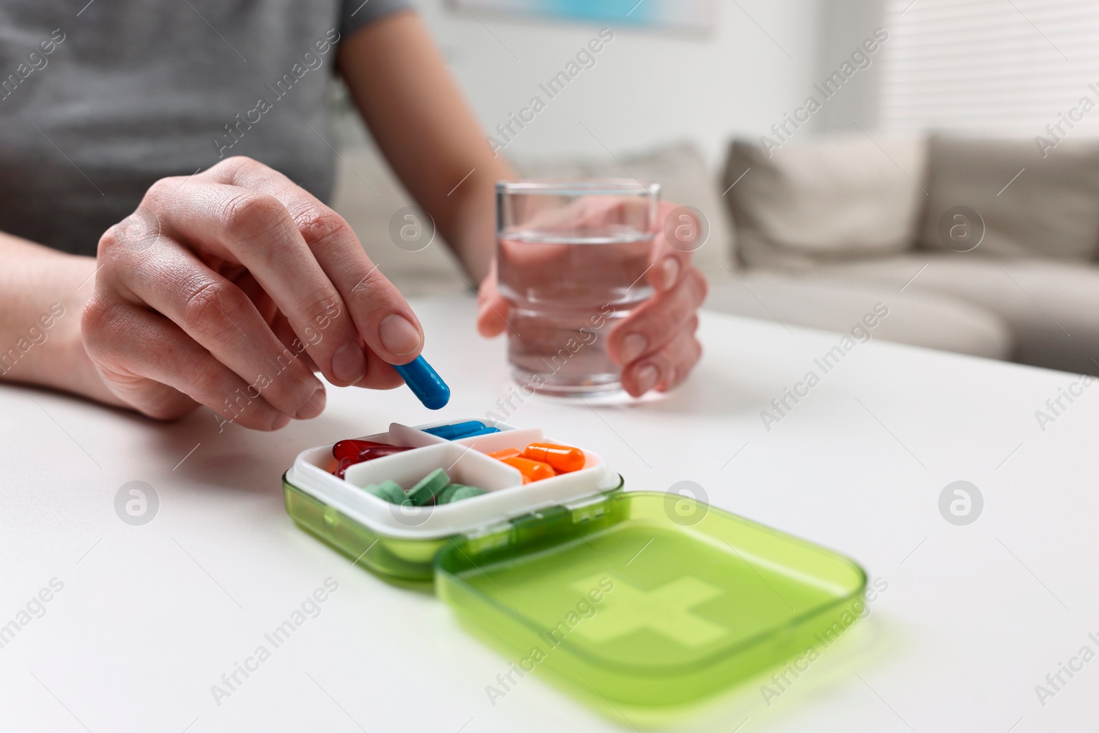 Photo of Woman with pills, organizer and glass of water at white table, closeup