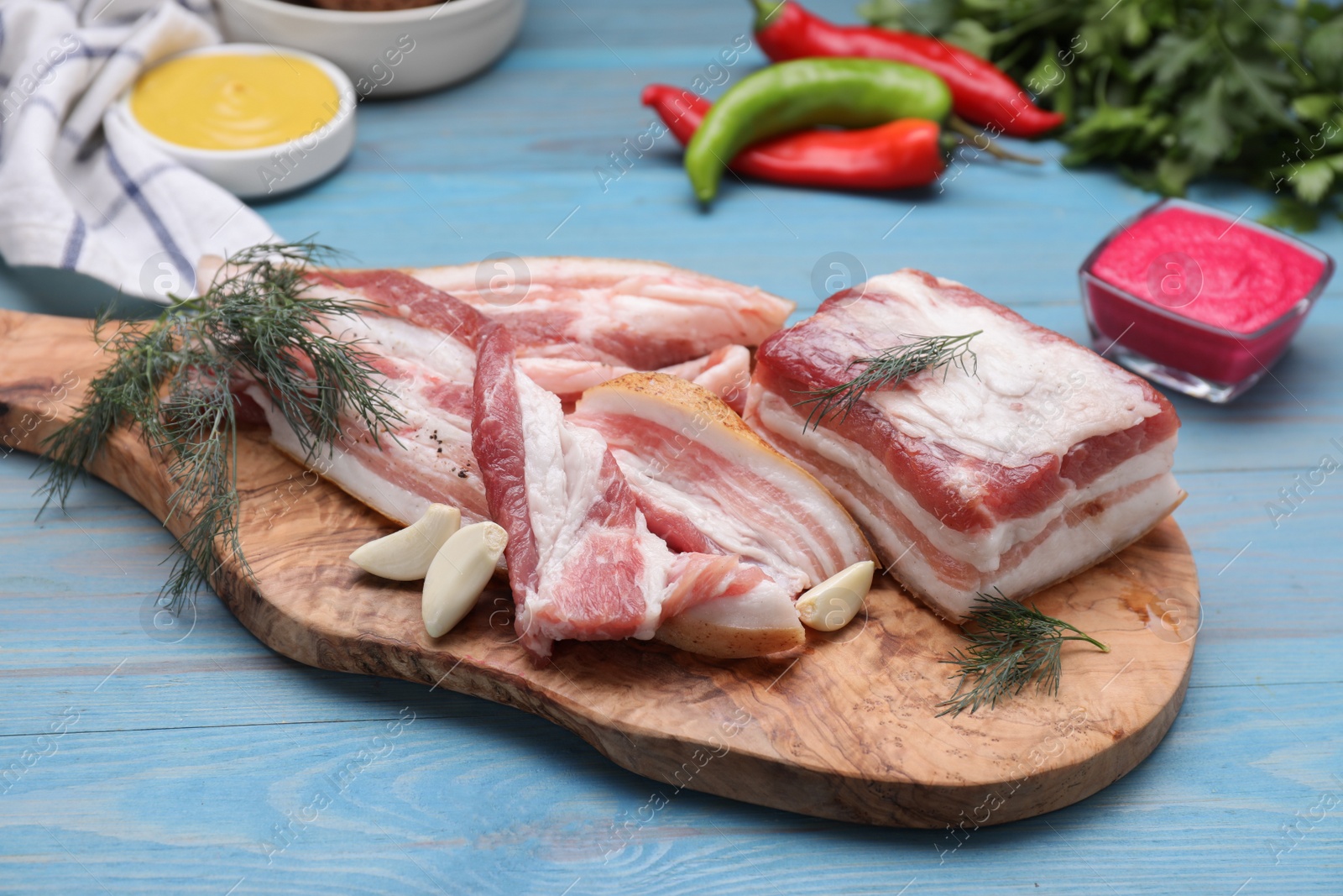 Photo of Pieces of pork fatback with garlic and dill on light blue wooden table