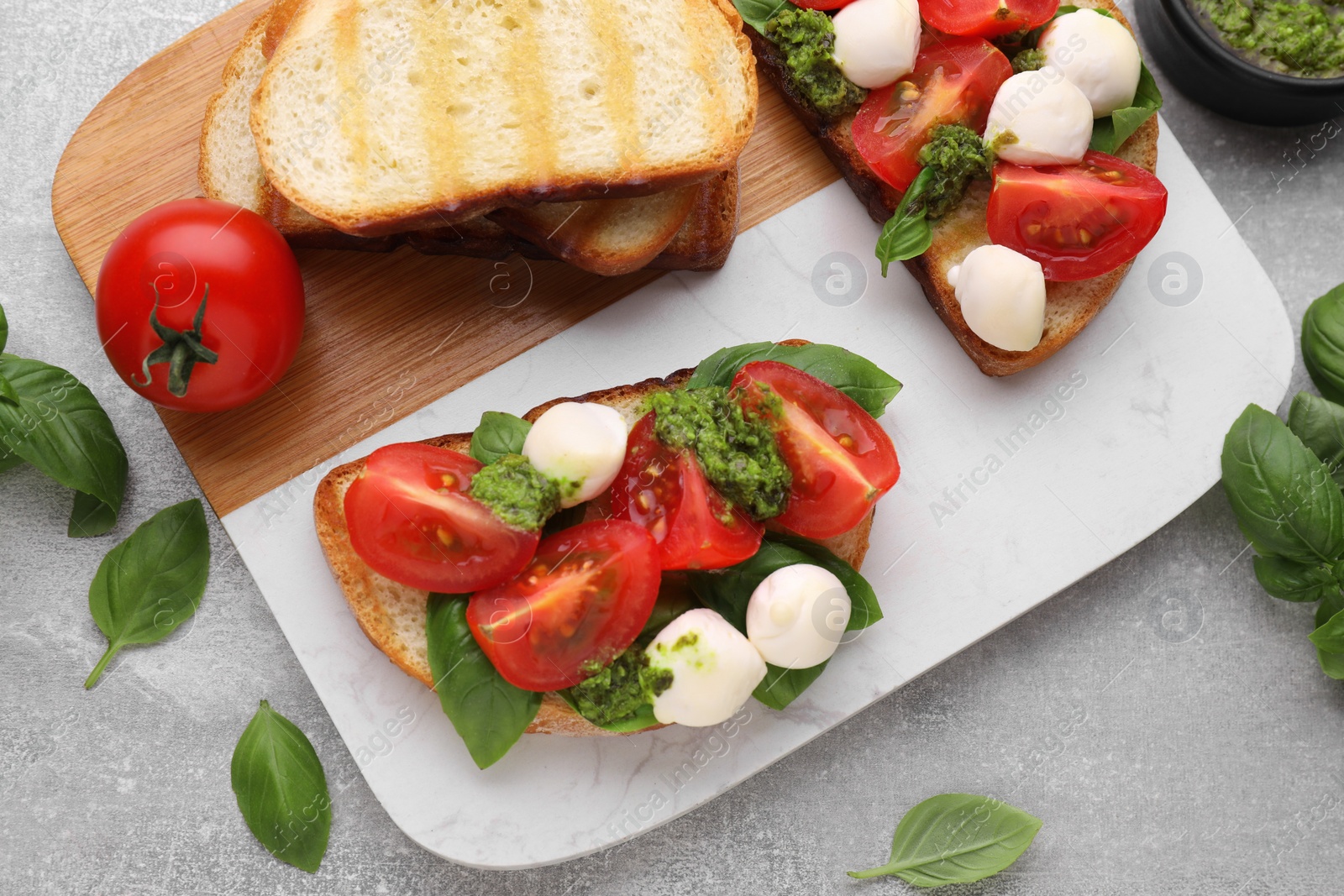 Photo of Delicious Caprese sandwiches with mozzarella, tomatoes, basil and pesto sauce on light grey table, flat lay