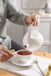 Photo of Woman pouring hot tea into cup at wooden table, closeup