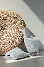 Photo of Pair of soft slippers and wicker pouf on floor near white wall