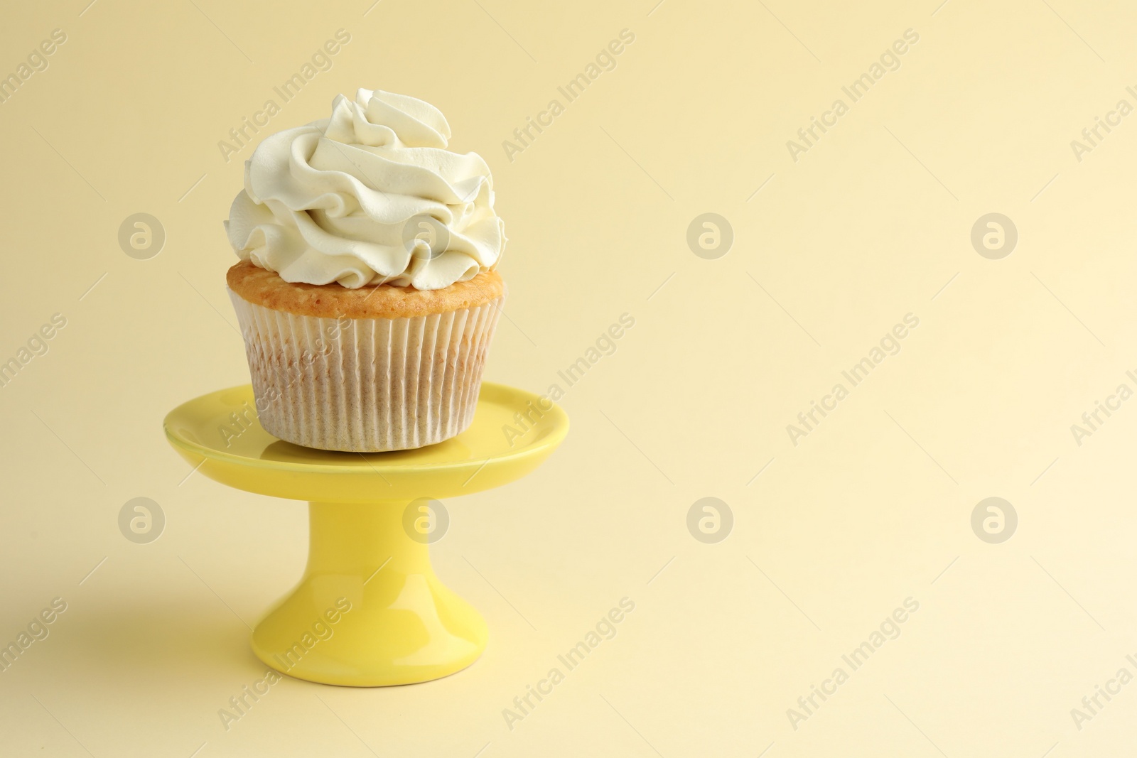 Photo of Tasty vanilla cupcake with cream on pale yellow background, space for text