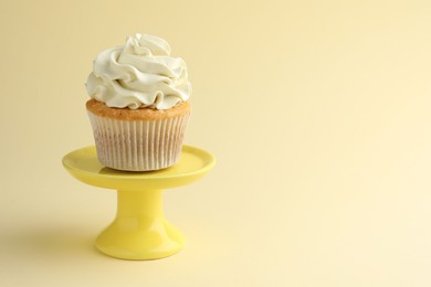 Tasty vanilla cupcake with cream on pale yellow background, space for text