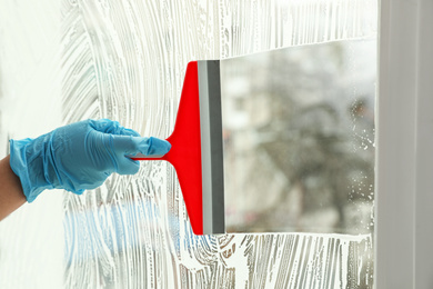 Woman cleaning window with squeegee indoors, closeup