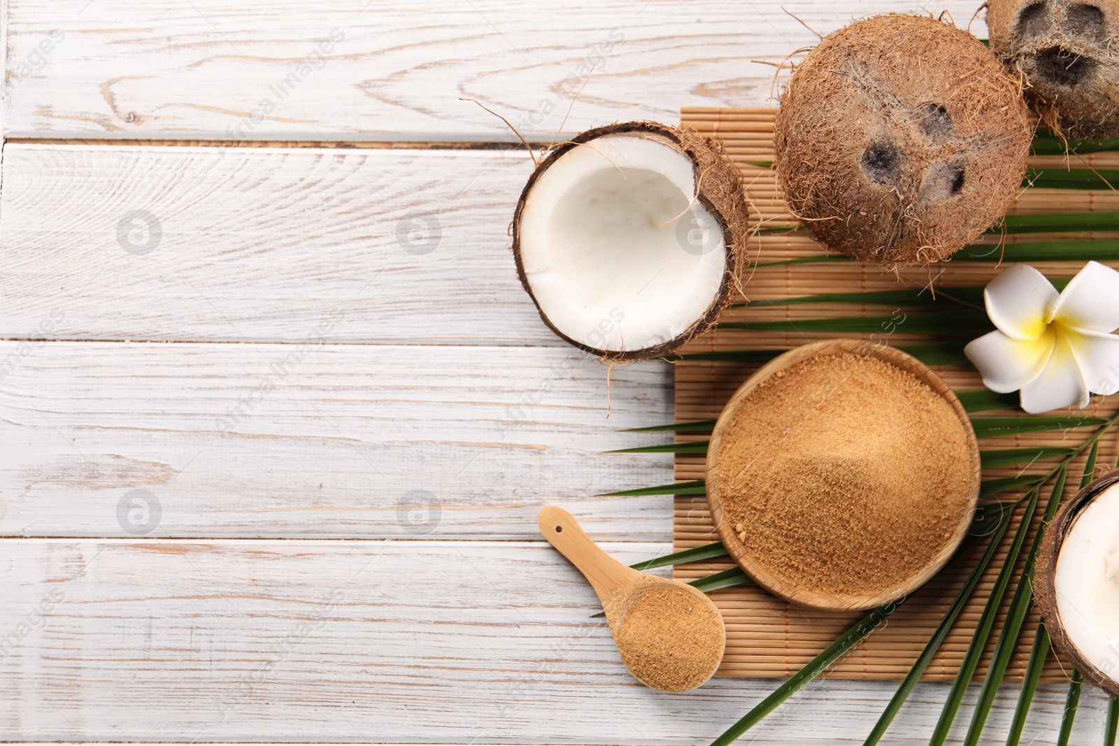 Photo of Coconut sugar, palm leaves, fruits and bamboo mat on wooden rustic table, flat lay. Space for text