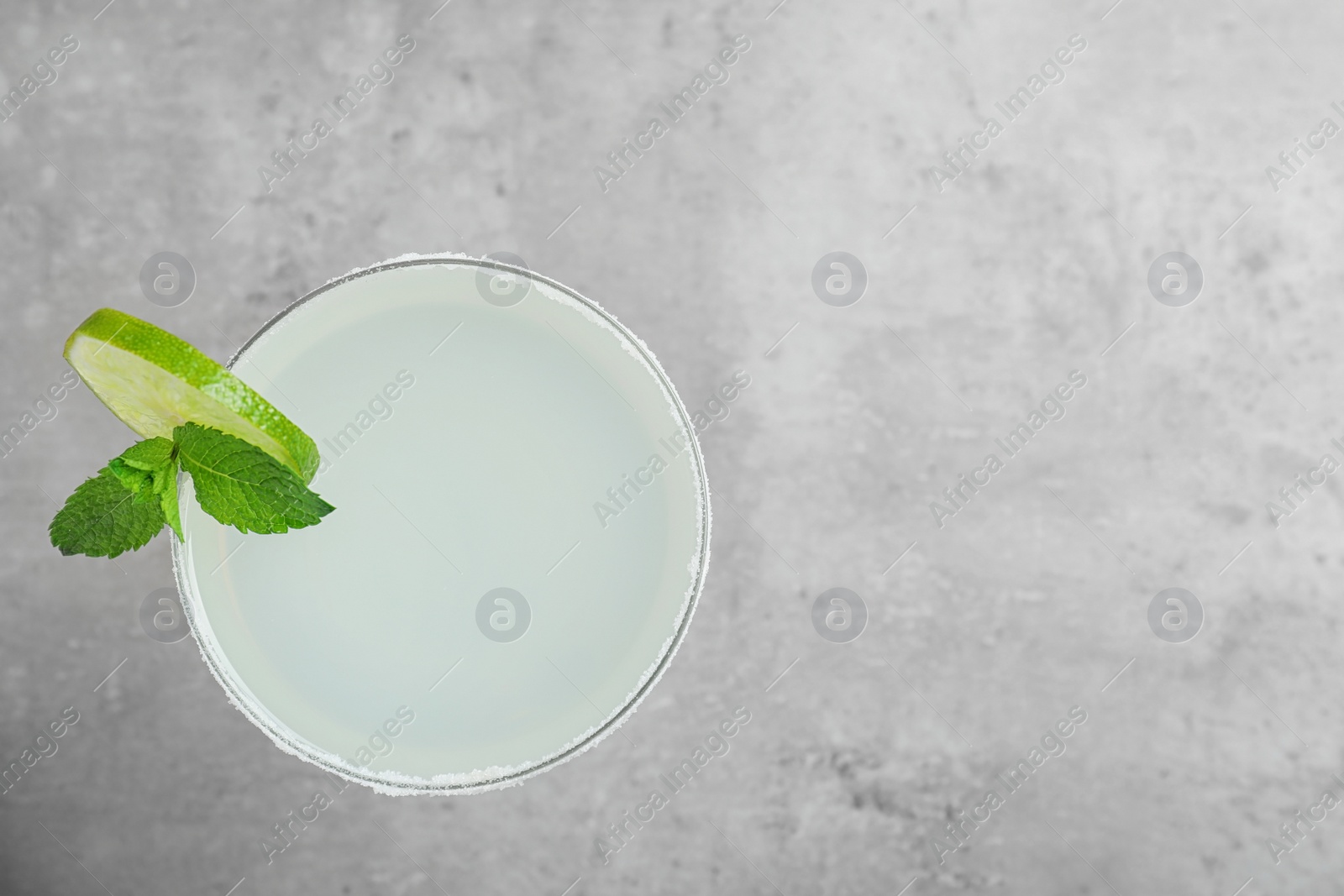 Photo of Glass of tasty refreshing cocktail with mint and lime on grey background, top view. Space for text