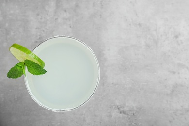 Photo of Glass of tasty refreshing cocktail with mint and lime on grey background, top view. Space for text