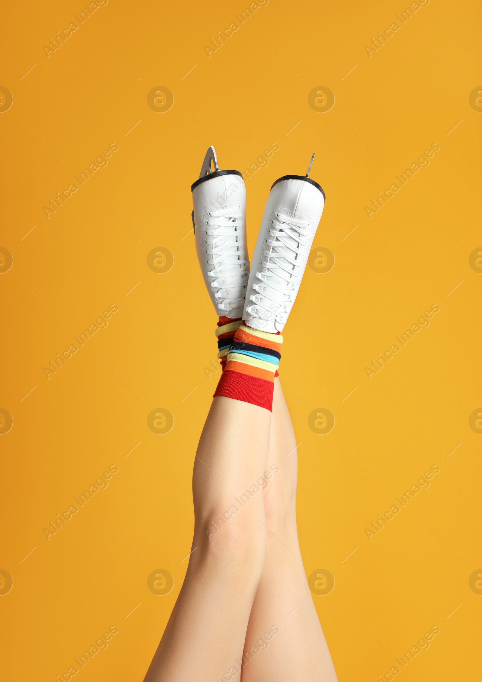 Photo of Woman in elegant white ice skates on yellow background, closeup of legs