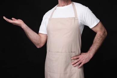 Man wearing kitchen apron on black background, closeup. Mockup for design